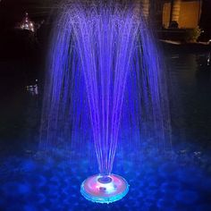 an illuminated fountain in the middle of a pond at night with blue lights on it