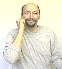 a man with a beard is holding his hand up to his ear and smiling at the camera