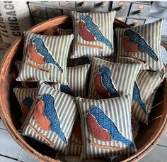 a basket filled with lots of pillows covered in blue and red birds sitting on top of each other