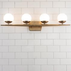 three lights are mounted on the wall next to a white brick wall in a bathroom