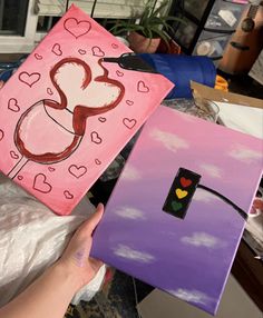 someone is holding up some paintings in their hands, one has a heart on it and the other has a stencil