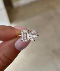 a woman's hand holding an engagement ring with two diamonds on top of it