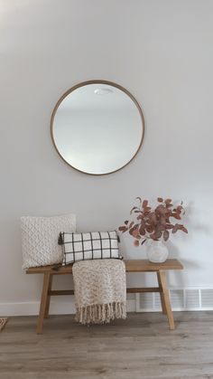 a wooden bench sitting under a round mirror next to a vase with flowers on it