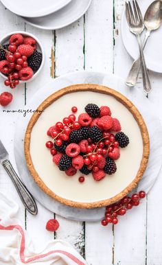 there is a pie with berries and cream in it on the table next to silverware