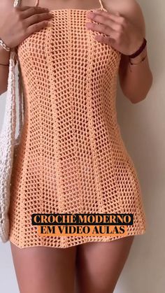 a woman is wearing an orange crochet dress and holding a white bag in her hand