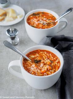 two white bowls filled with soup on top of a gray tablecloth next to silver spoons