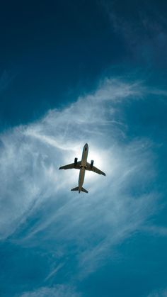 an airplane is flying through the blue sky with white clouds in the foreground and sun behind it