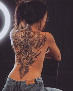 a woman sitting in front of a mirror with her back turned to the camera and tattoos on her body