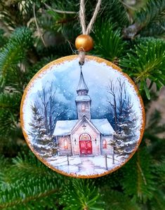 a christmas ornament hanging from a tree with snow on the ground and a church in the background