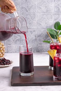 someone pouring red wine into two glasses on a tray next to pineapples and other fruit