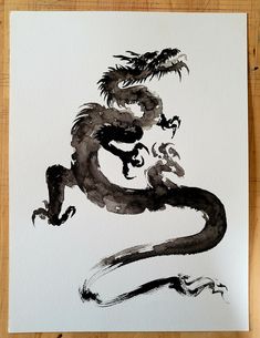 a black and white painting of a dragon sitting on top of a piece of paper