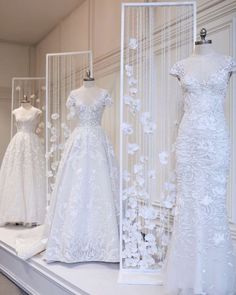 wedding gowns are displayed on display in a shop window, with white flowers all over them