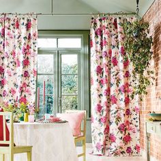 a dining room with pink flowers on the curtains and table in front of a brick wall