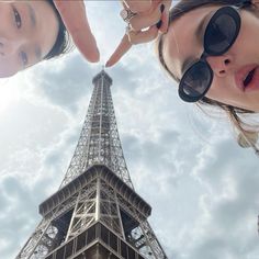 two people standing next to each other in front of the eiffel tower, looking up into the sky