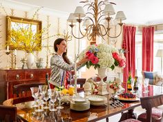 a woman arranging flowers in a vase on top of a dining room table with plates and glasses