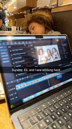 an open laptop computer sitting on top of a wooden table next to a woman sleeping