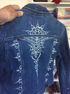 the back of a denim jacket with white embroidered designs on it, being held up by someone's hand