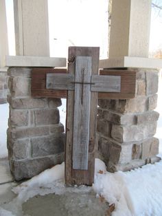 a wooden cross sitting in the snow next to a brick wall and window sill