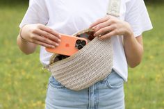 a woman is holding an orange cell phone in her purse while standing on the grass