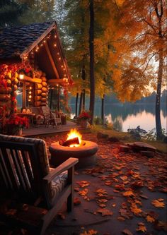 a fire pit in front of a log cabin with autumn leaves on the ground and trees around it