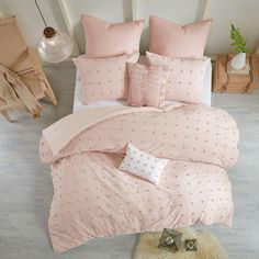 a bed with pink comforters and pillows in a white room next to a window