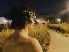 a shirtless man standing on a sidewalk at night with his back turned to the camera