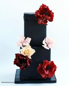 a three tiered black cake with red and white flowers on the top, sitting in front of a white background