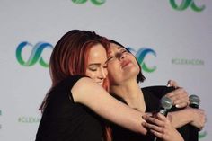 two women hugging each other while holding a microphone