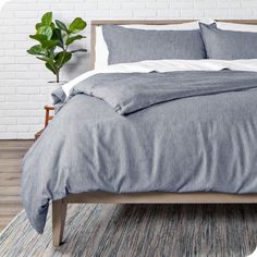 a bed with blue linens and pillows in a white brick wall bedroom, next to a potted plant