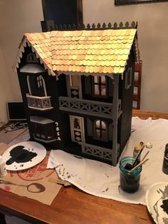 a doll house sitting on top of a wooden table next to paint and paper plates