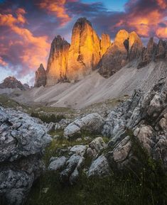 the mountains are covered in rocks and grass as the sun sets over them, with pink clouds