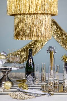 A table with a champagne bottle and glasses, adorned with Meri Meri's Gold Tinsel Chandelier. Tinsel Chandelier, Holiday Event Decor, Fringe Garland, Handmade Halloween Decorations, Gold Party Decorations, Christmas Party Themes, Tinsel Garland, Glitter Party, Glitter Ribbon