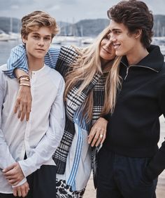 two boys and a girl standing next to each other in front of water with boats