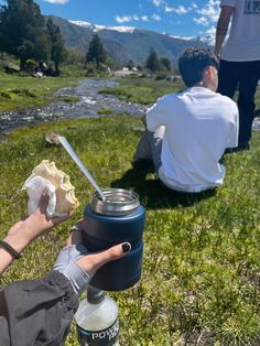 a person sitting in the grass with a hot dog and water bottle next to them