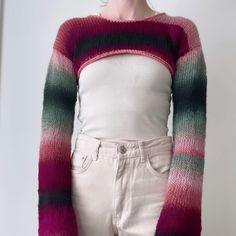 a woman standing in front of a white wall wearing a pink and green striped sweater