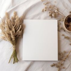 there is a blank paper next to some dried flowers and a cup on the bed