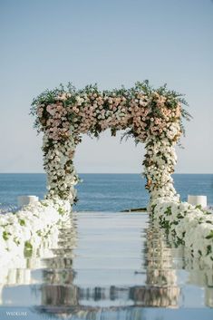 an outdoor ceremony setup with flowers and greenery on the water's edge, overlooking the ocean