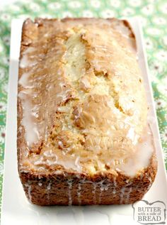 a loaf of banana bread with icing on a white plate and green floral tablecloth