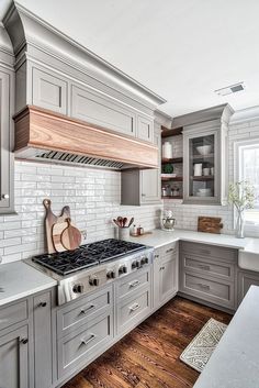 a kitchen with gray cabinets and white tile backsplash, wooden cutting board on the stove