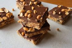 several pieces of chocolate peanut butter bars stacked on top of each other with nuts scattered around them