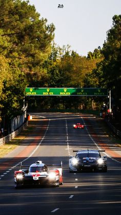 two race cars driving down the road in front of an overpass with a green sign above it