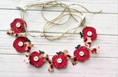 a necklace made out of red flowers with white buttons and bows on it, sitting on a wooden surface