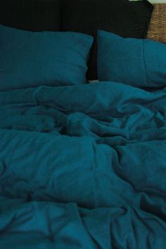 an unmade bed with dark blue sheets and pillows on top of the headboard