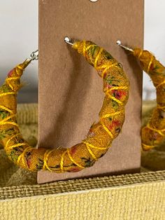 a pair of yellow hoop earrings sitting on top of a cardboard box next to a card