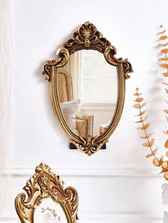 an ornate gold framed mirror on the wall next to a vase with flowers in it