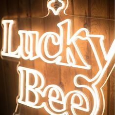 a neon sign that says lucky bee on it's side in front of a wooden wall