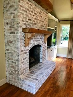 a brick fireplace in the middle of a living room with wood flooring and windows