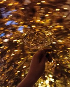 a hand holding a wine glass in front of a gold glittered ceiling at night