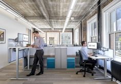 two men working in an office setting with desks and computer screens on the wall