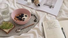 a bowl of cereal and an open book on a bed next to a glass of water